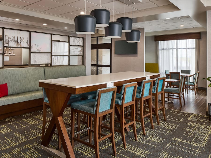 A hotel lobby with a seating area, a long table with chairs, and a large window.