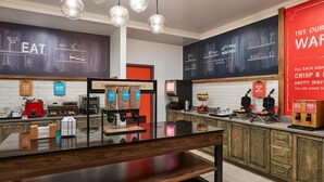 A modern kitchen with a central island, a chalkboard wall with cooking-related drawings, and a red wall with a waffle advertisement. - Hampton Inn Colby (Colby)
