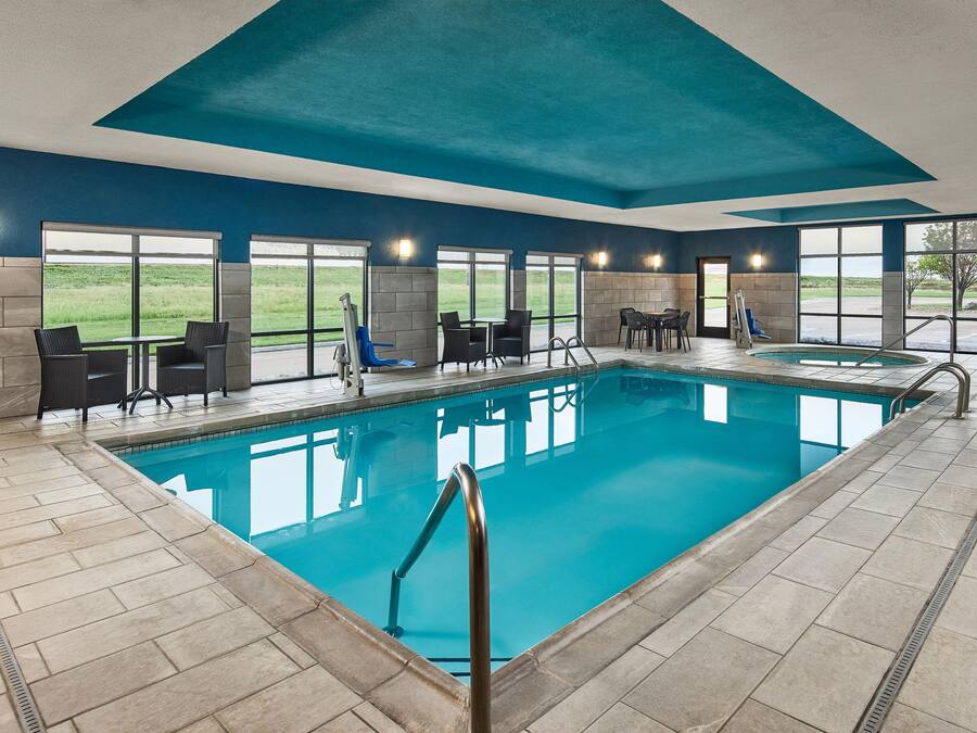 An indoor swimming pool with clear blue water, surrounded by seating areas and large windows offering views of the outdoors.