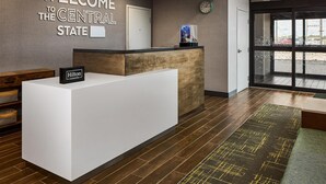 A hotel reception area with a 'Welcome to the Central State' sign, a clock, and a Hilton Honors sign on the reception desk. - Hampton Inn Colby (Colby)