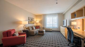 A hotel room with a sofa, armchair, desk, and television.