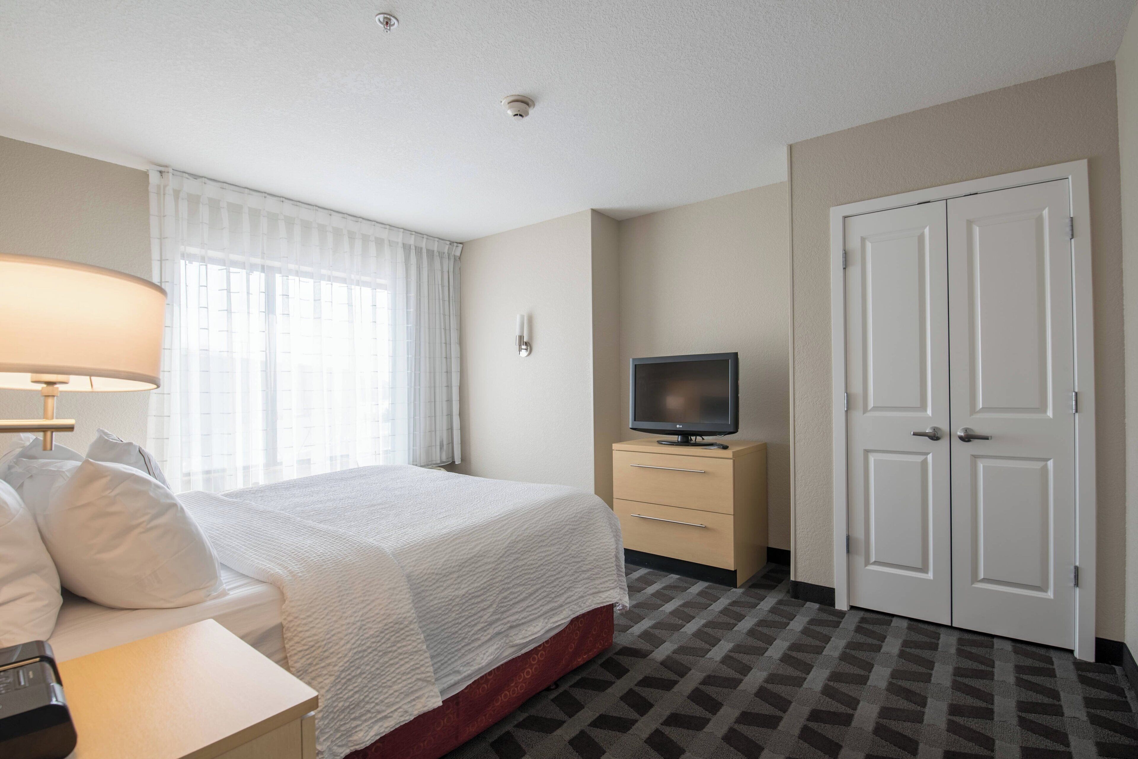 A hotel room with a bed, a TV on a stand, a desk, and a wardrobe.