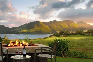 Un foyer extérieur avec une table et des chaises, offrant une vue sur un terrain de golf et les montagnes.