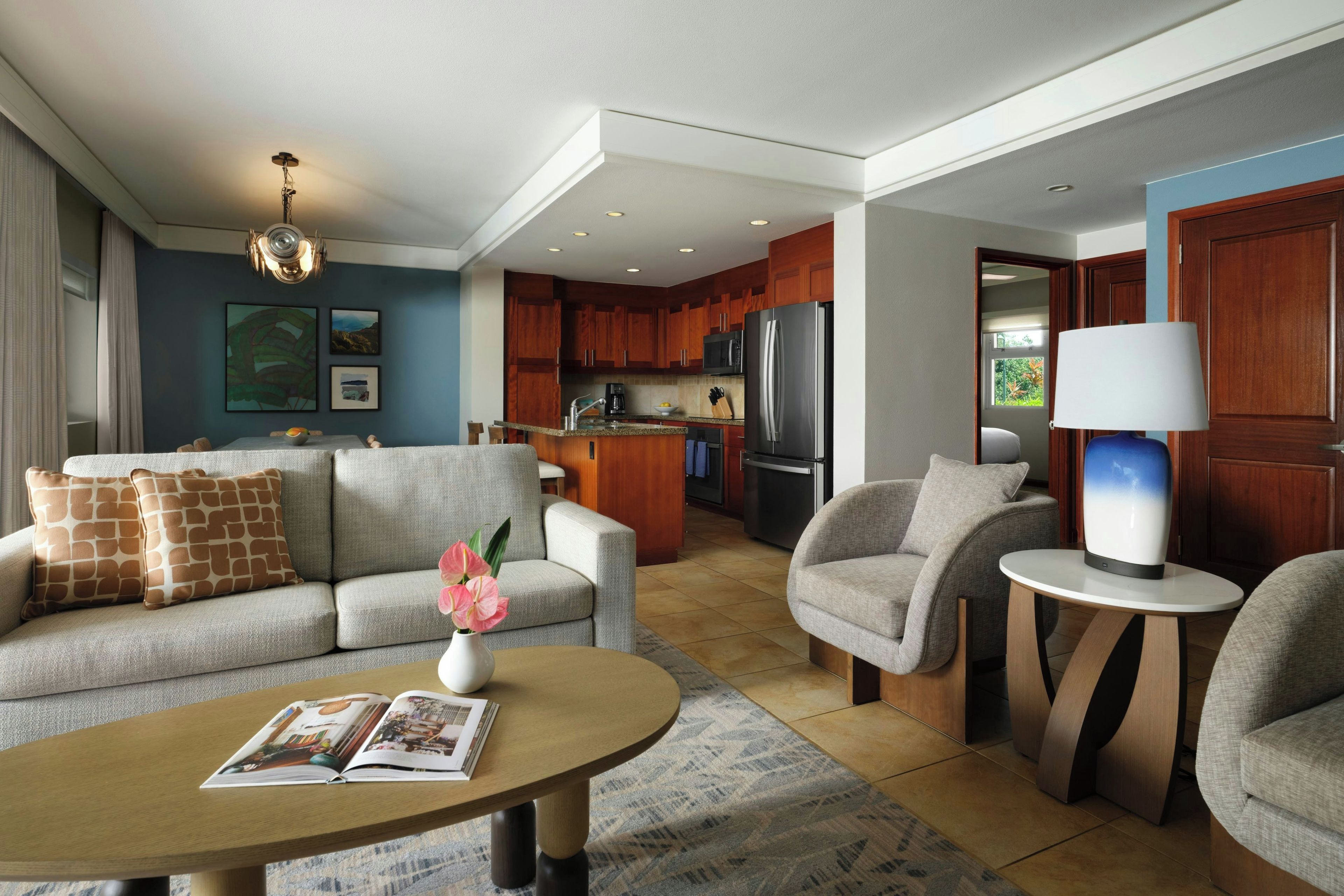 A modern living room with a sofa, armchairs, a coffee table, and a dining area with a kitchen in the background.