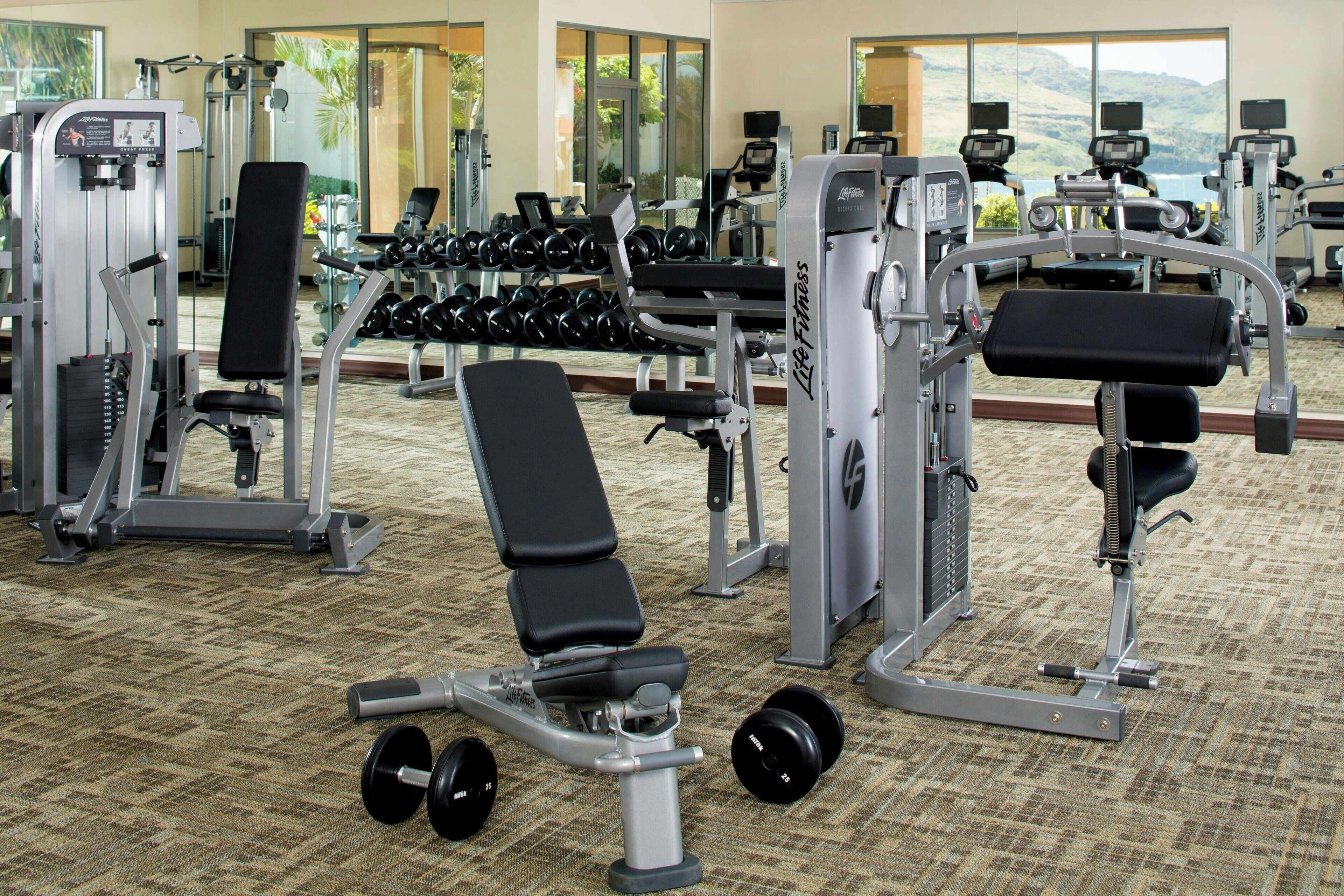 A gym with various exercise machines, dumbbells, and benches.