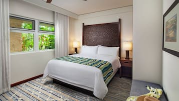 Una habitación de hotel con cama, ventana con cortinas, ventilador de techo y mesita de noche con lámpara.