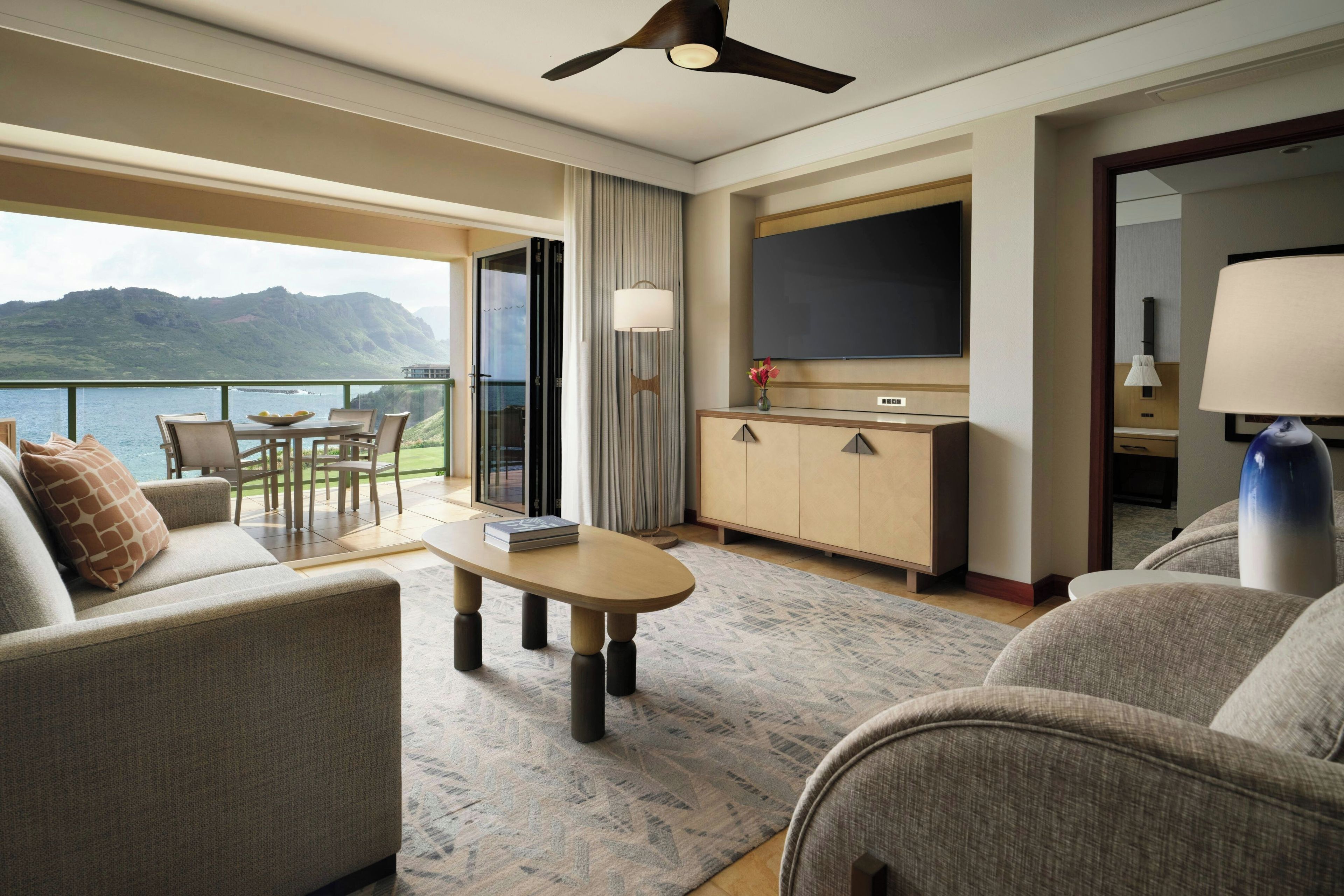 Una habitación de hotel con balcón, sofá, mesa de centro, televisor y armario.