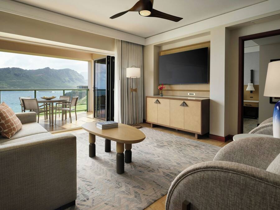 Una habitación de hotel con balcón, sofá, mesa de centro, televisor y armario.