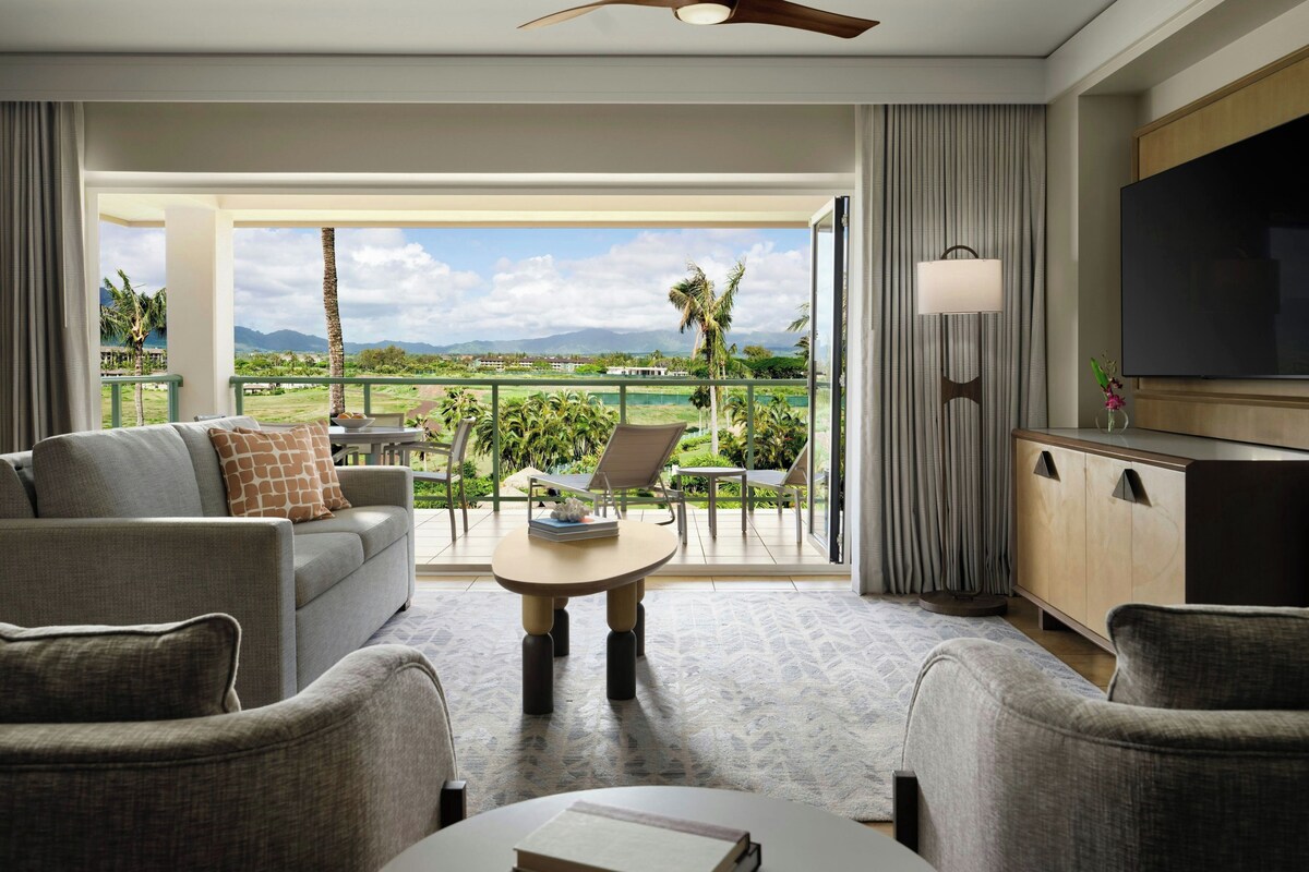 A hotel room with a balcony, a sofa, a coffee table, a TV, and a cabinet.