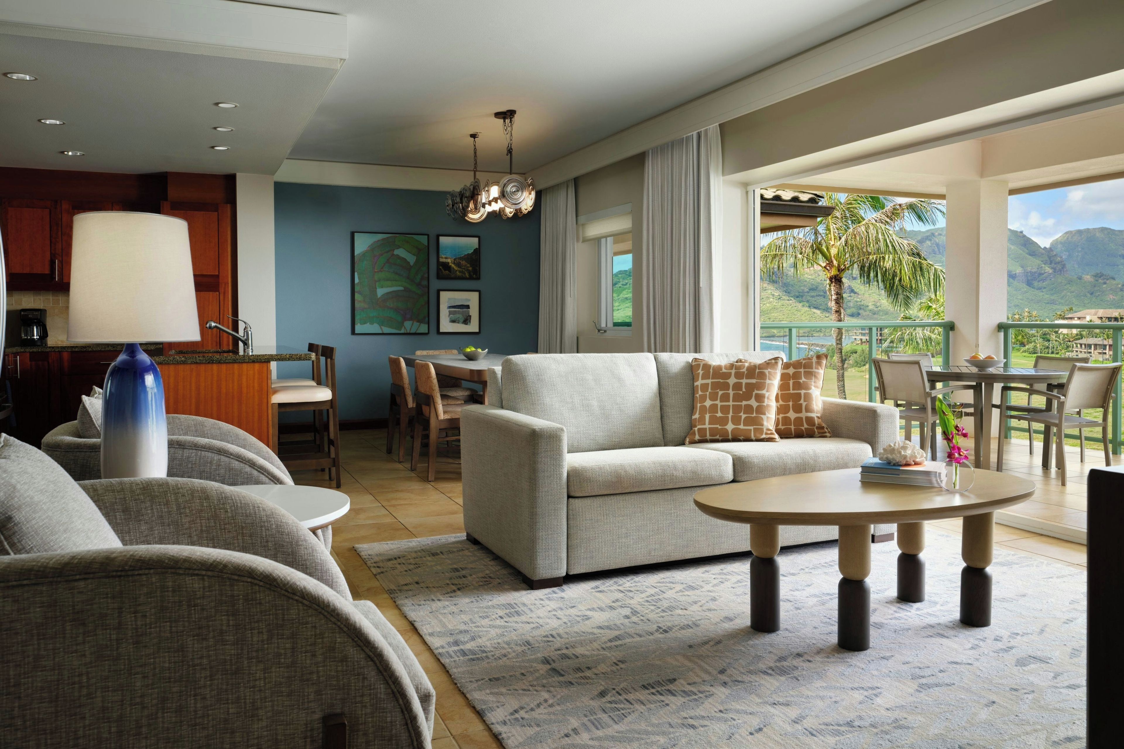 A modern living room with a sofa, chairs, a coffee table, and a view of a mountainous landscape through large windows.