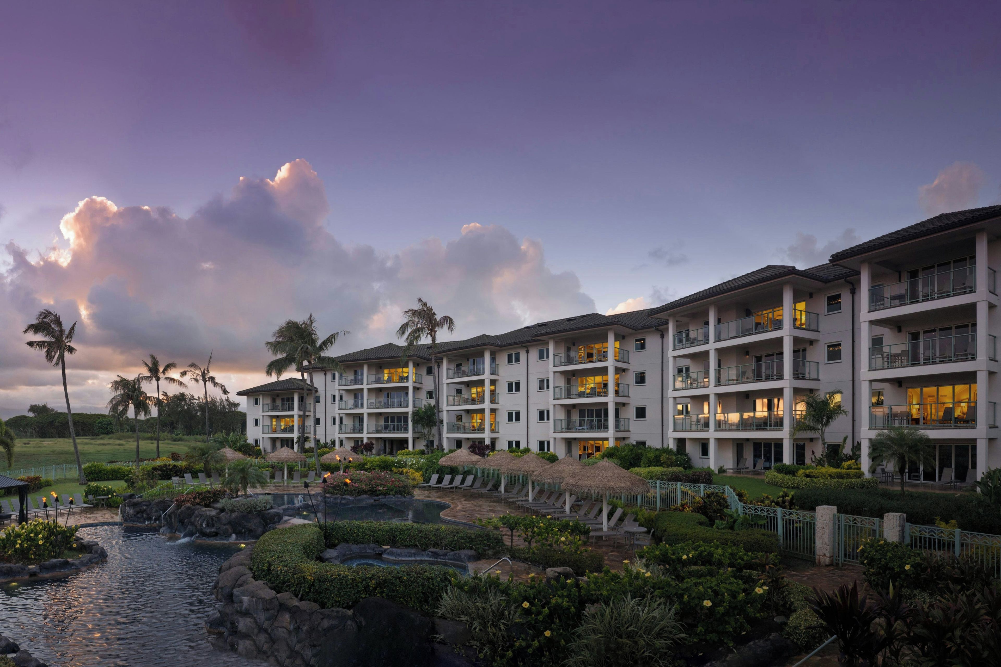 A multi-story hotel with balconies, a swimming pool, and tropical landscaping.