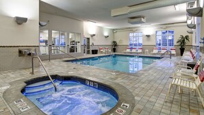 An indoor swimming pool with a hot tub, lounge chairs, and a tiled floor.
