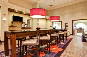 Un vestíbulo de hotel con zona de bar, asientos y televisor.