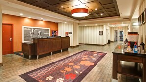 A hotel reception area with a wooden reception desk, a large floral rug, and a modern ceiling design.