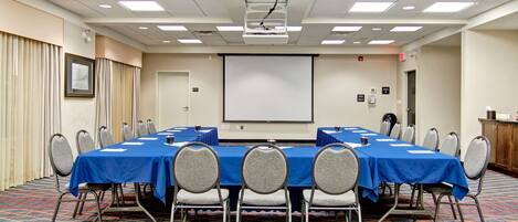 A conference room with a long table, chairs, a projector screen, and a carpeted floor.