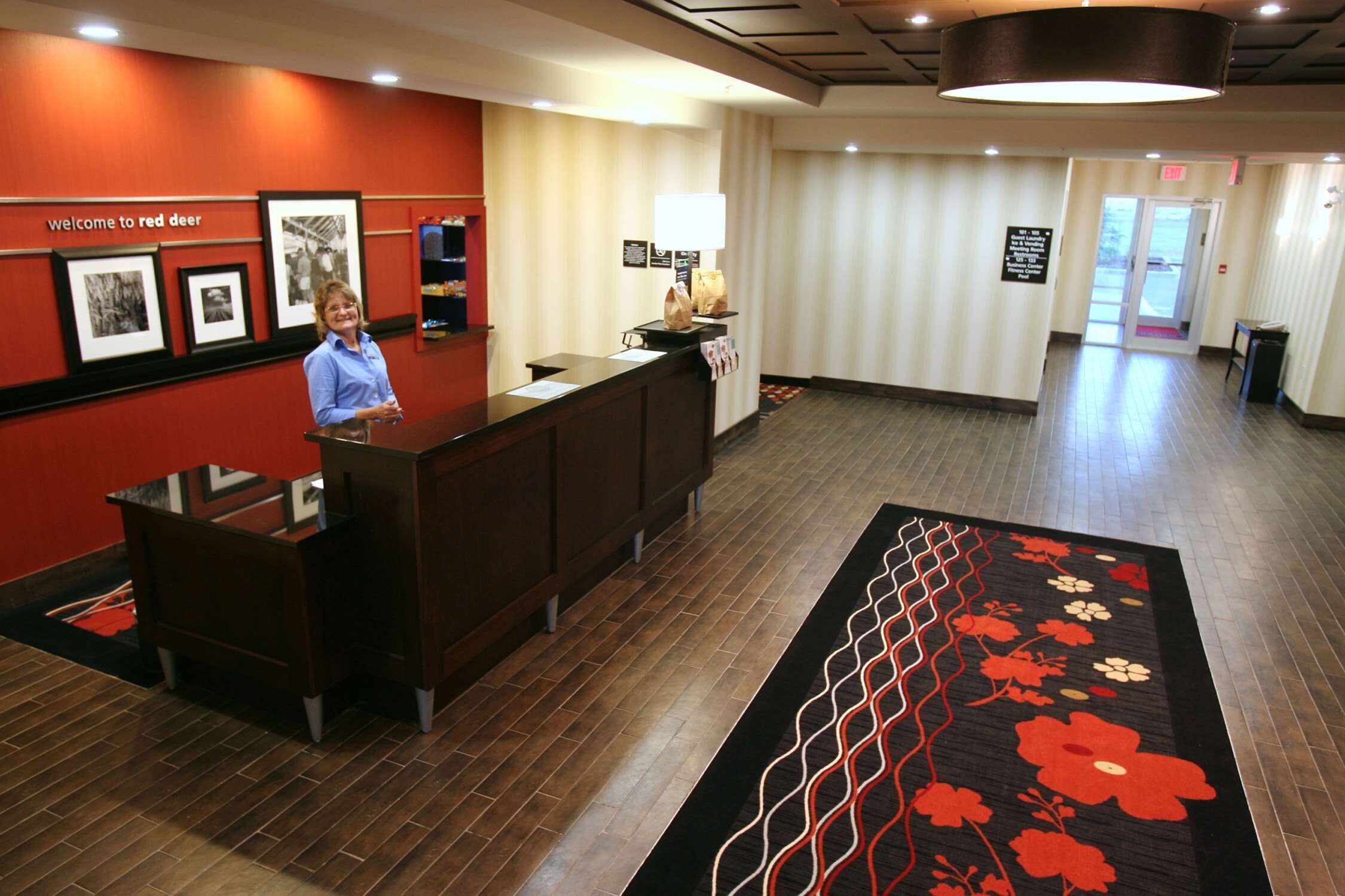 Un área de recepción con un mostrador de madera, cuadros en la pared y una alfombra roja que conduce a la salida.