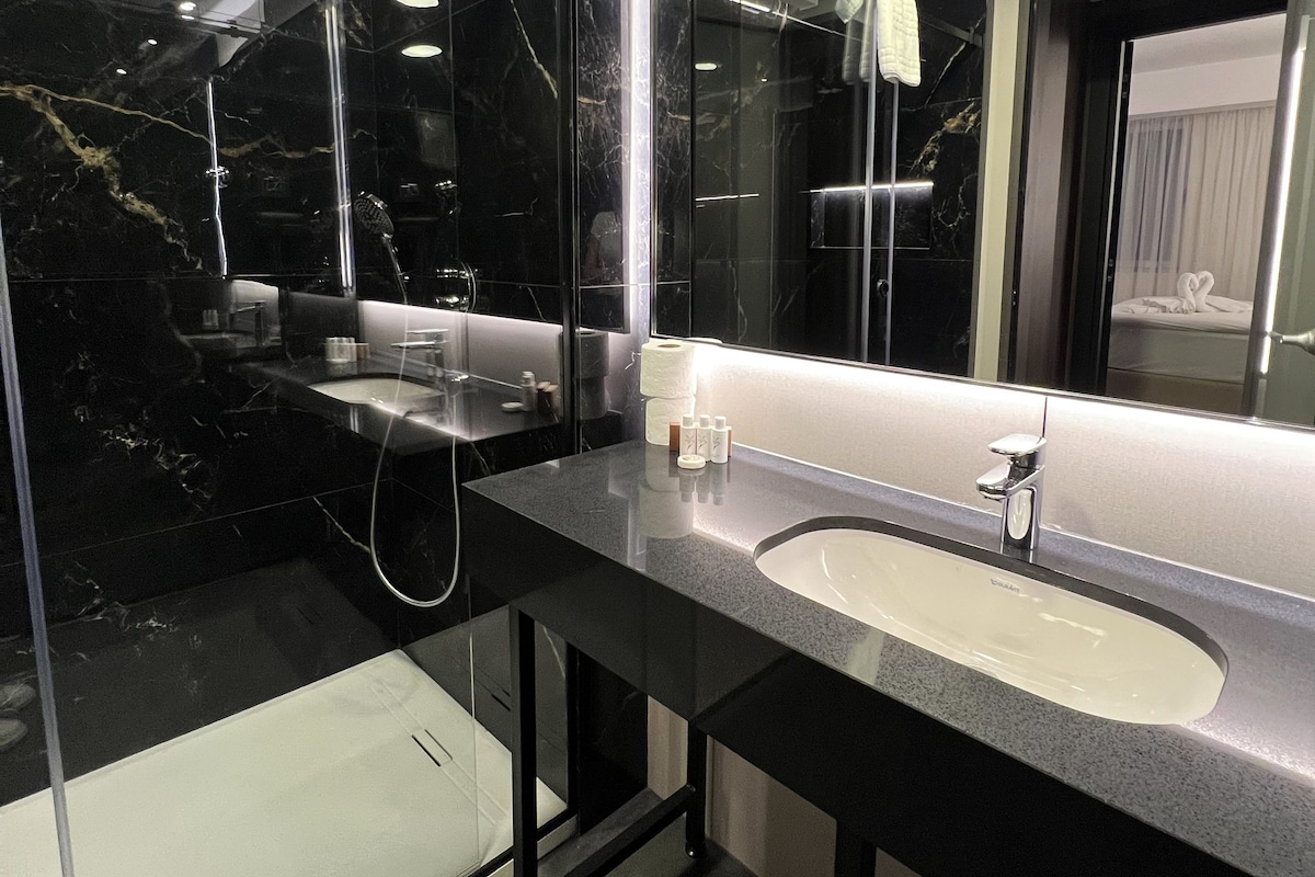 A modern bathroom with a black marble vanity, a large mirror, and a separate shower area.