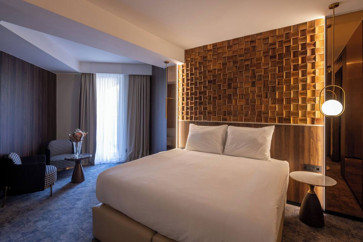 A hotel room with a large bed, a wooden accent wall, a round table, and a sofa.