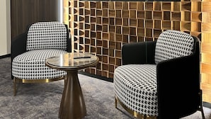 A modern room with a geometric patterned wall, two houndstooth patterned chairs, and a round table. - Nobel Design (Belgrade)