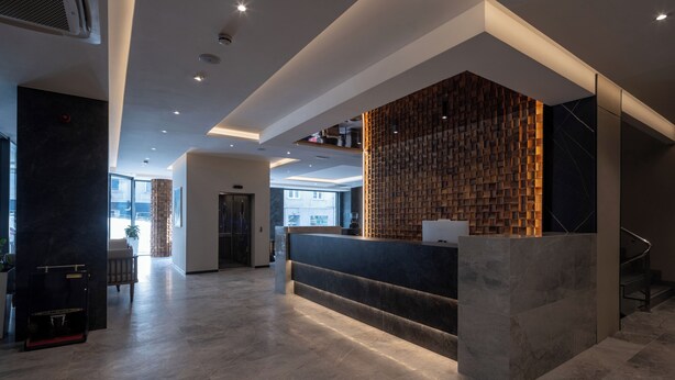 A modern reception area with a marble counter, a wooden wall feature, and a view of the outside. - Nobel Design (Belgrade)