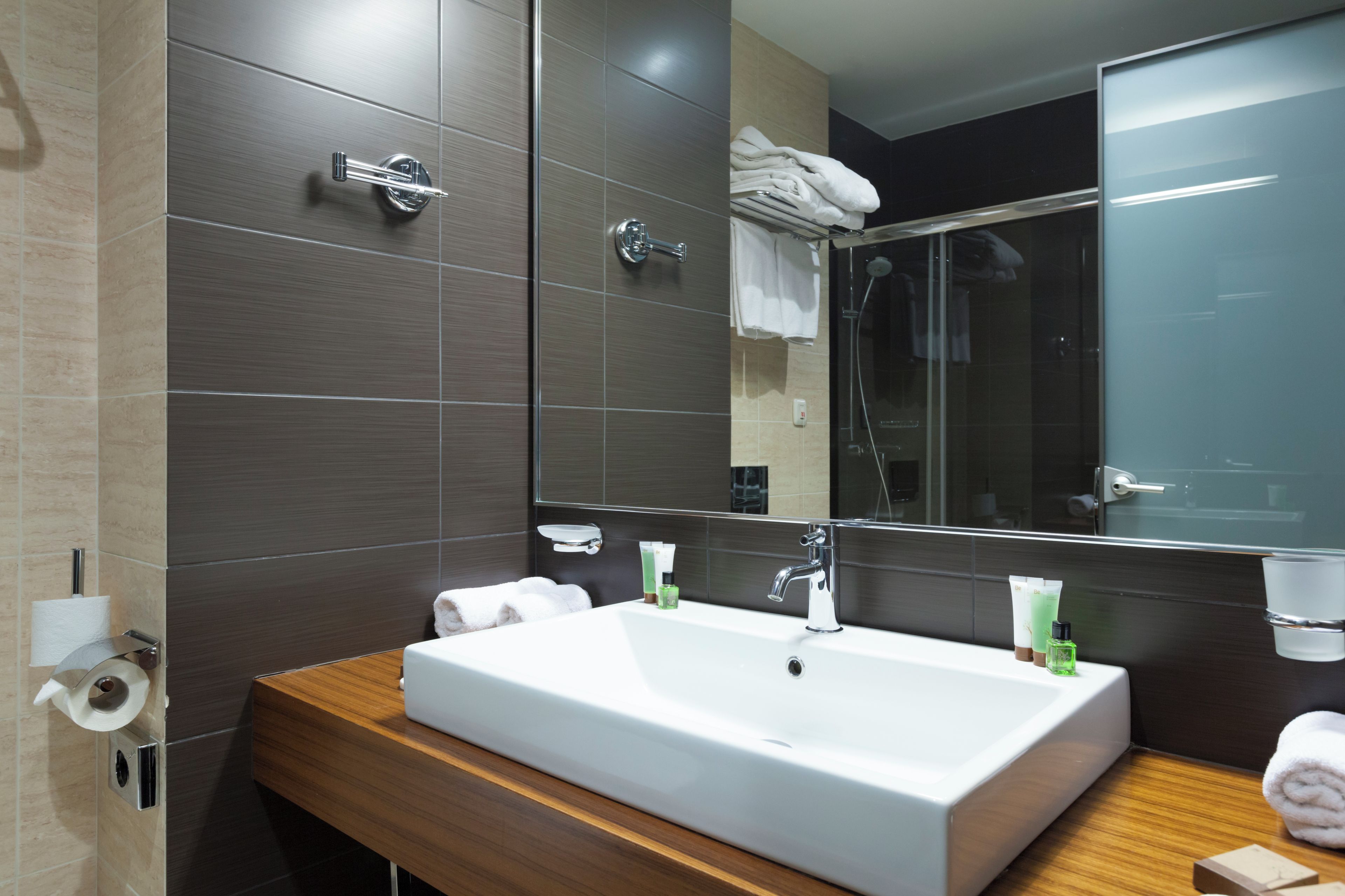 A modern bathroom with a large mirror, a white sink, and a wooden vanity.
