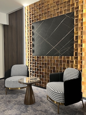 A modern room with a geometric patterned wall, two houndstooth patterned chairs, and a round table.