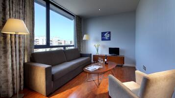 Una sala de estar moderna con un sofá, una mesa de centro, un televisor y vistas a la ciudad a través de amplias ventanas.