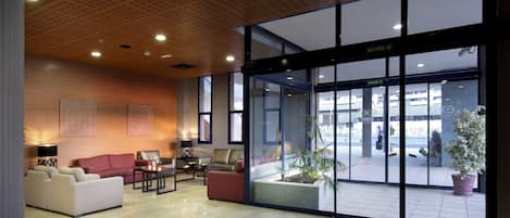 Un hall d’entrée moderne doté d’un espace salon, d’une grande entrée vitrée et d’un plafond orné d’un motif géométrique.