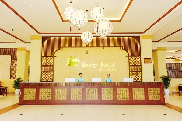 A reception area with a wooden reception desk, two receptionists, and a large sign reading "Sunny Beach Resort & Spa".