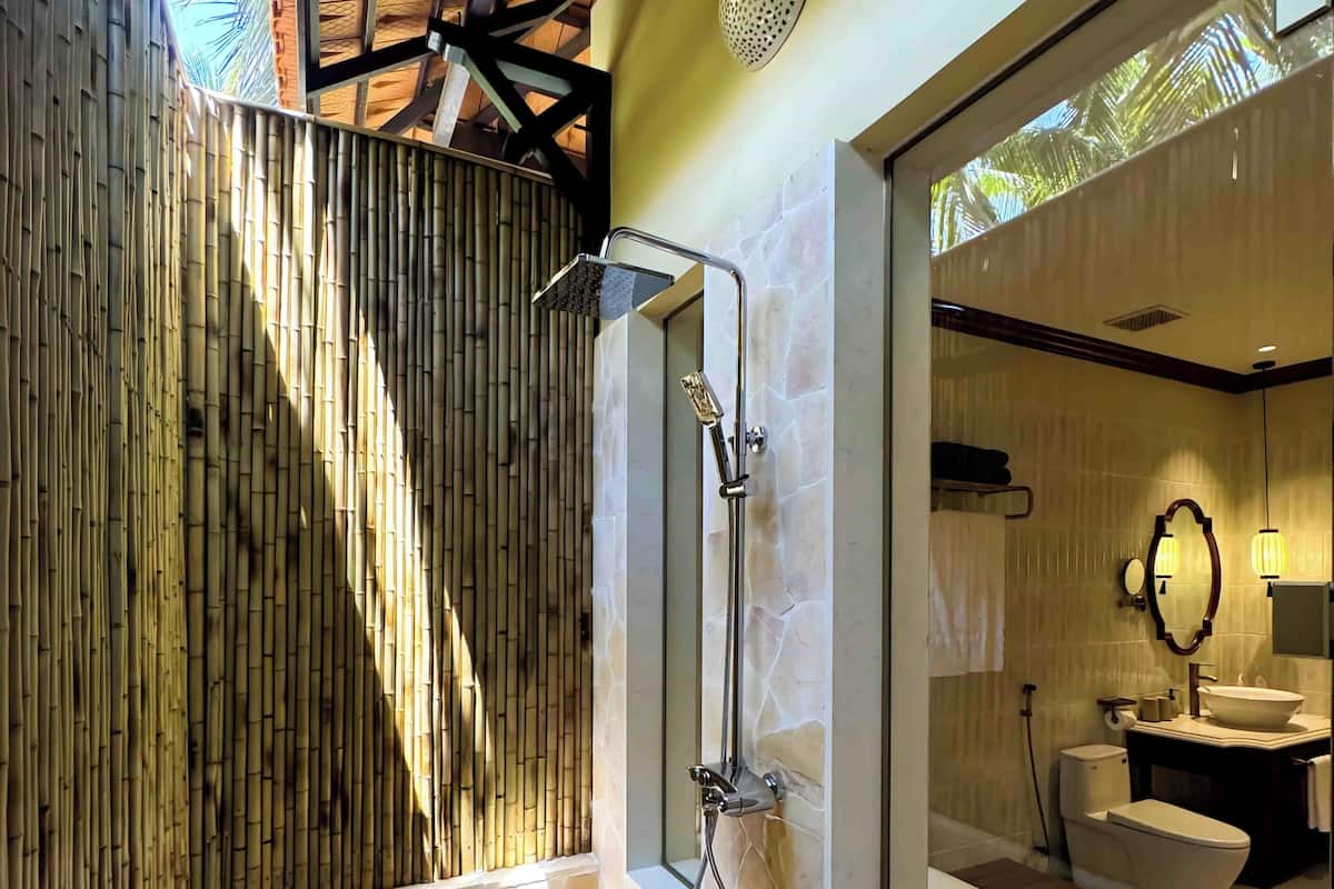 A modern bathroom with a stone bathtub, a shower with a handheld showerhead, a large mirror, and a view of the outside.