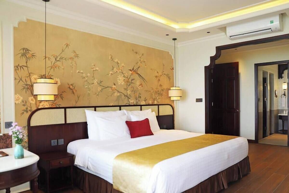 A hotel room with a large bed, a nightstand, a wall with floral wallpaper, and a door leading to a bathroom.