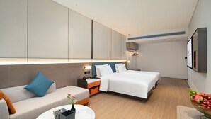 Una habitación de hotel moderna con sofá, dos camas, una mesita de noche, una pequeña mesa con un florero y un frutero.