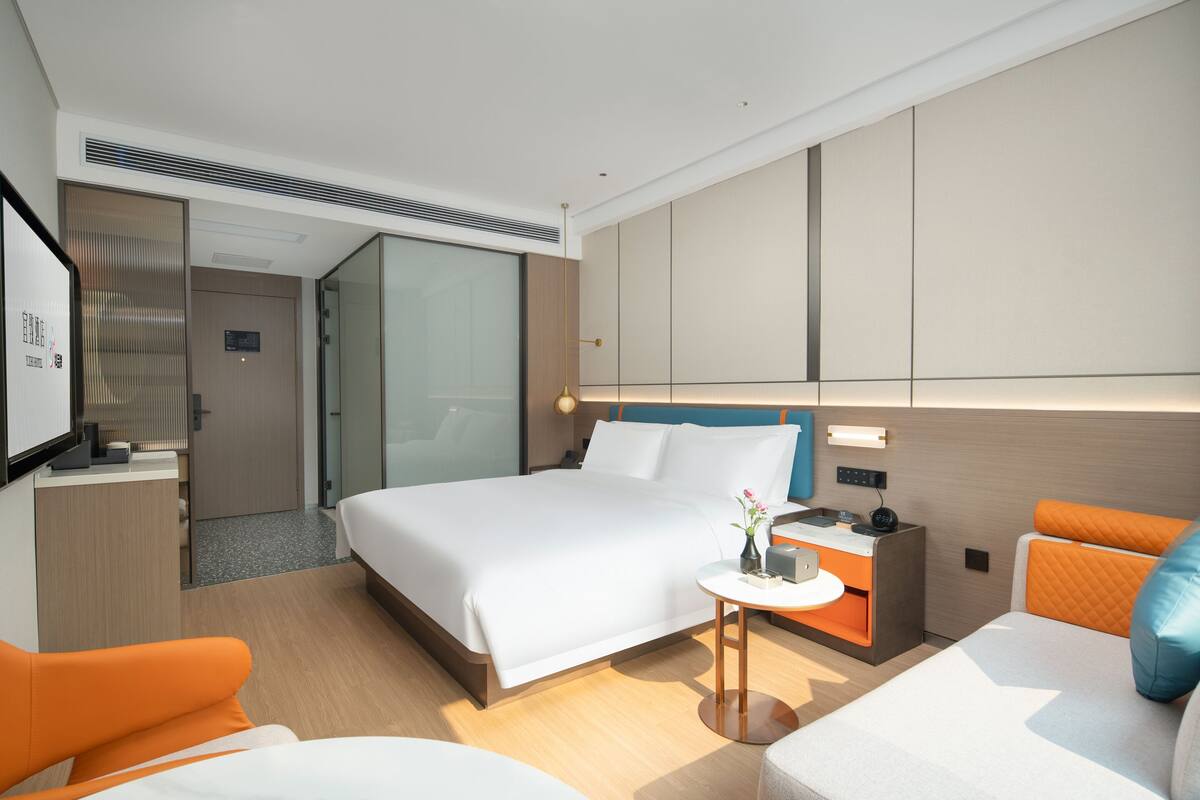 Ein modernes Hotelzimmer mit einem großen Bett, einem Schreibtisch, einem Sessel und einem kleinen Tisch mit einer Vase.