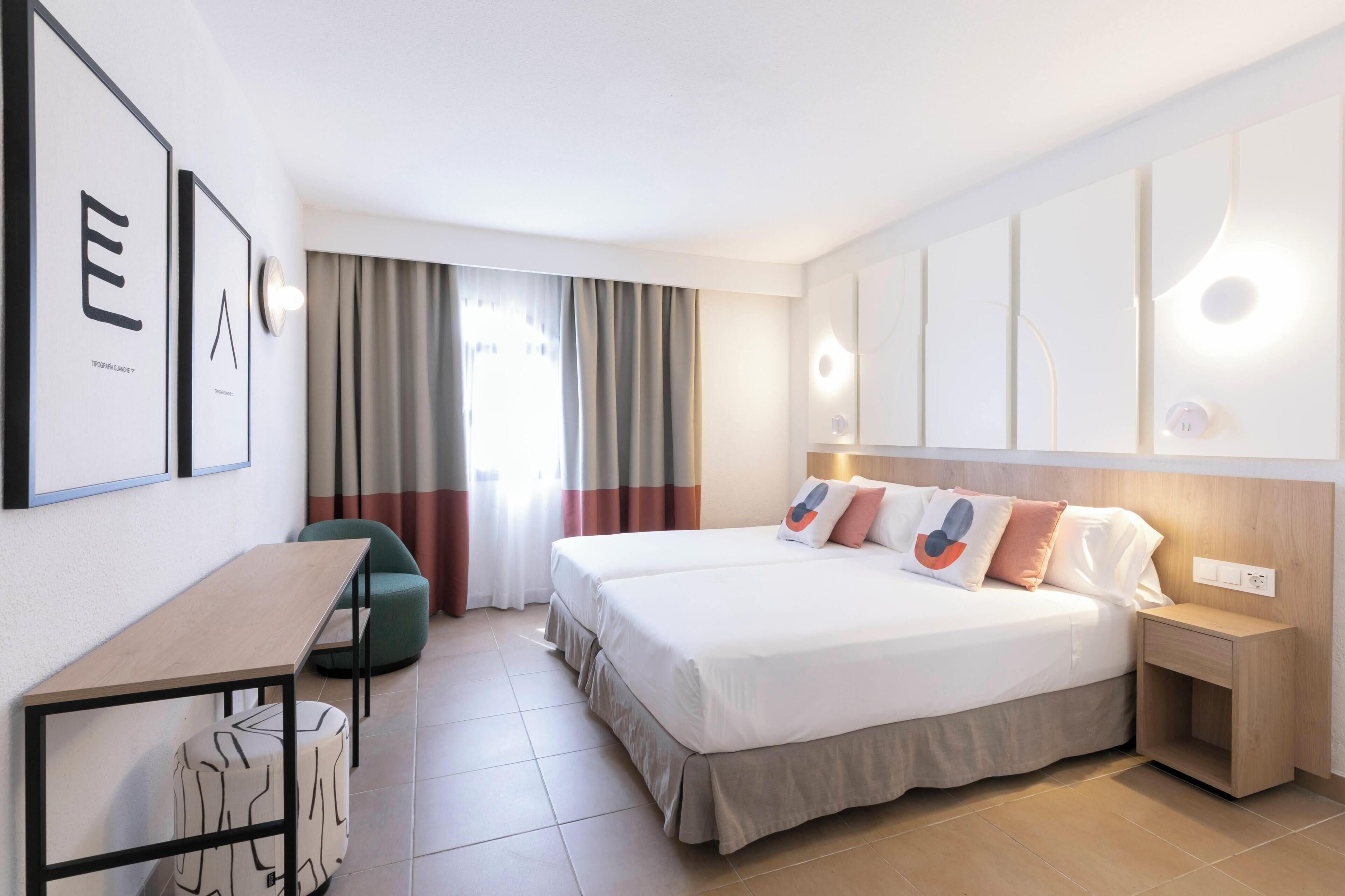 Una habitación de hotel moderna con una cama, mesita de noche y un escritorio con silla.