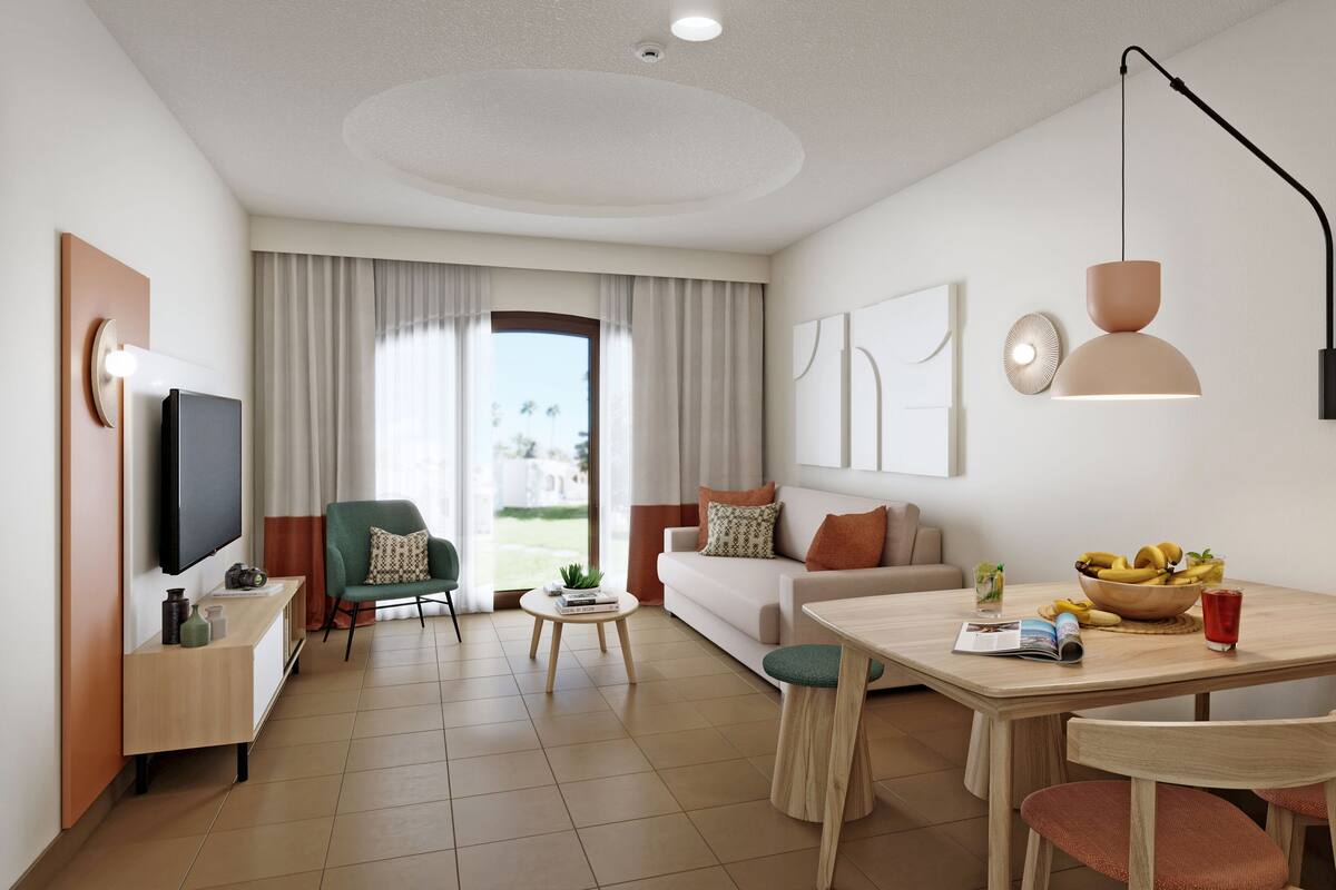 Une chambre d’hôtel moderne dotée d’une télévision à écran plat, d’un coin repas avec une table et des chaises, d’un canapé et d’un balcon avec des rideaux.