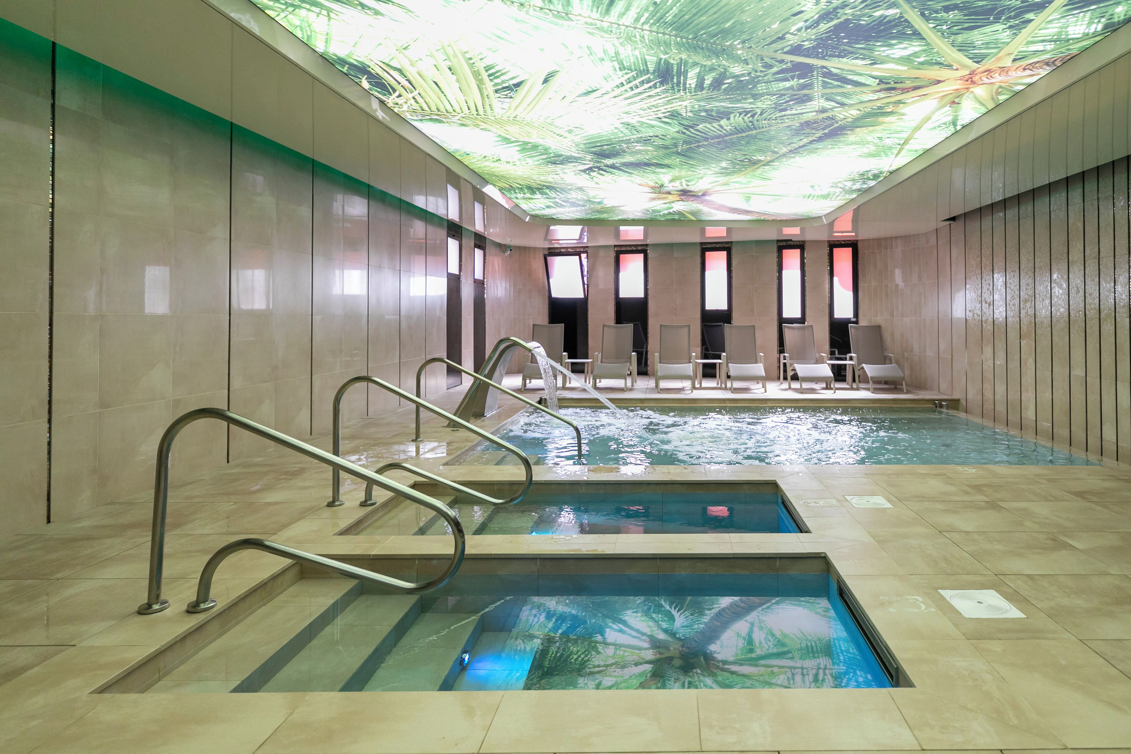 Una piscina con un mural en el techo, paredes de azulejos y algunas sillas de descanso.