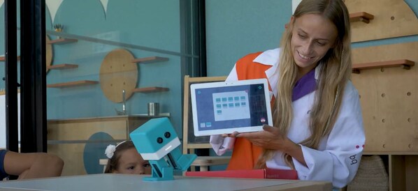 A person holding a tablet in a room with a large window, wooden furniture, and a wall-mounted shelf.