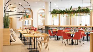 Een modern restaurant met houten tafels en rode stoelen, met een lange toonbank met een bankje en hangplanten.