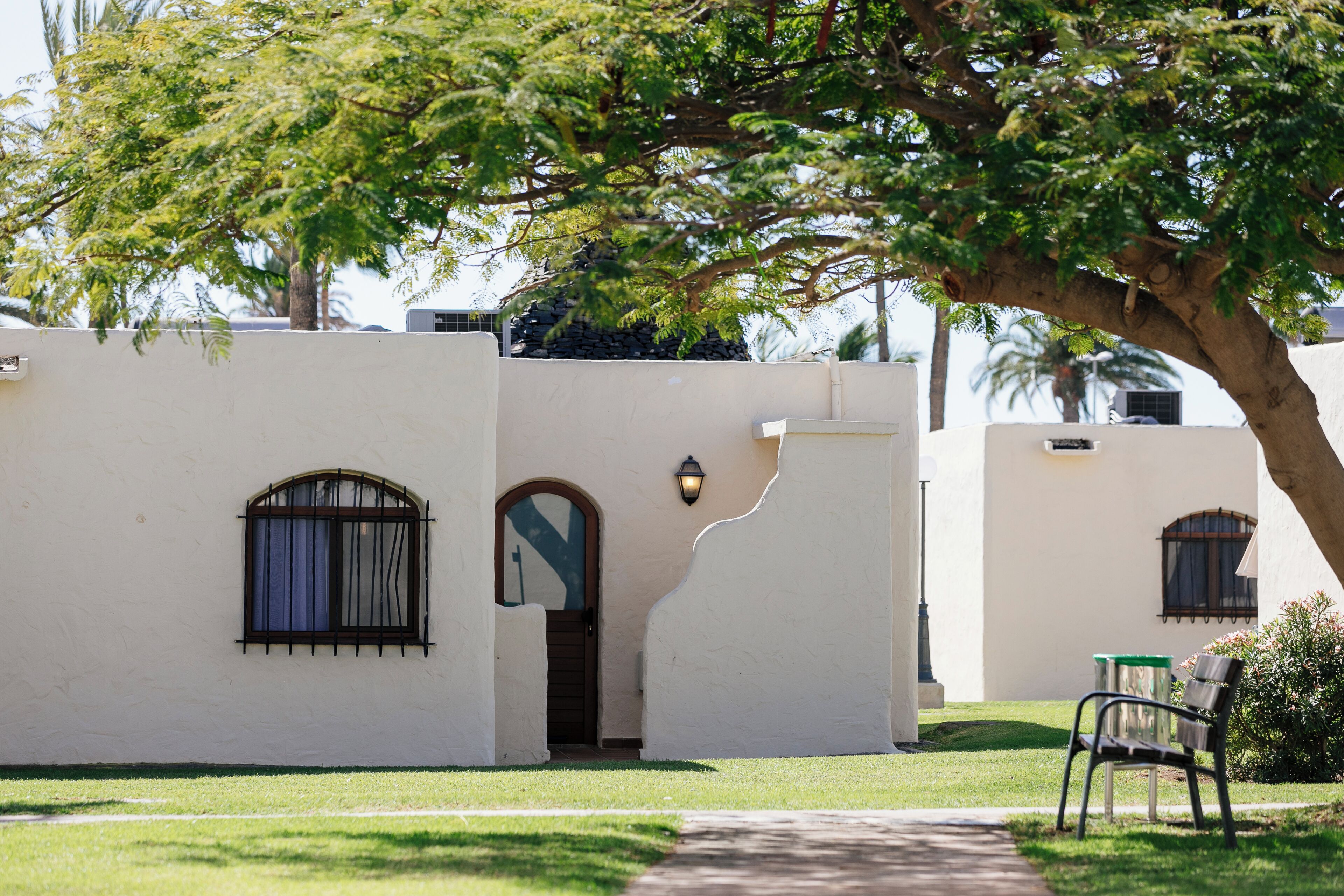 Un edificio de fachada blanca, una pequeña entrada con puerta de madera y una ventana con reja de metal.
