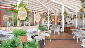 Un espace patio intérieur aménagé avec des meubles en osier blanc, des lampes en osier suspendues et des plantes en pot.