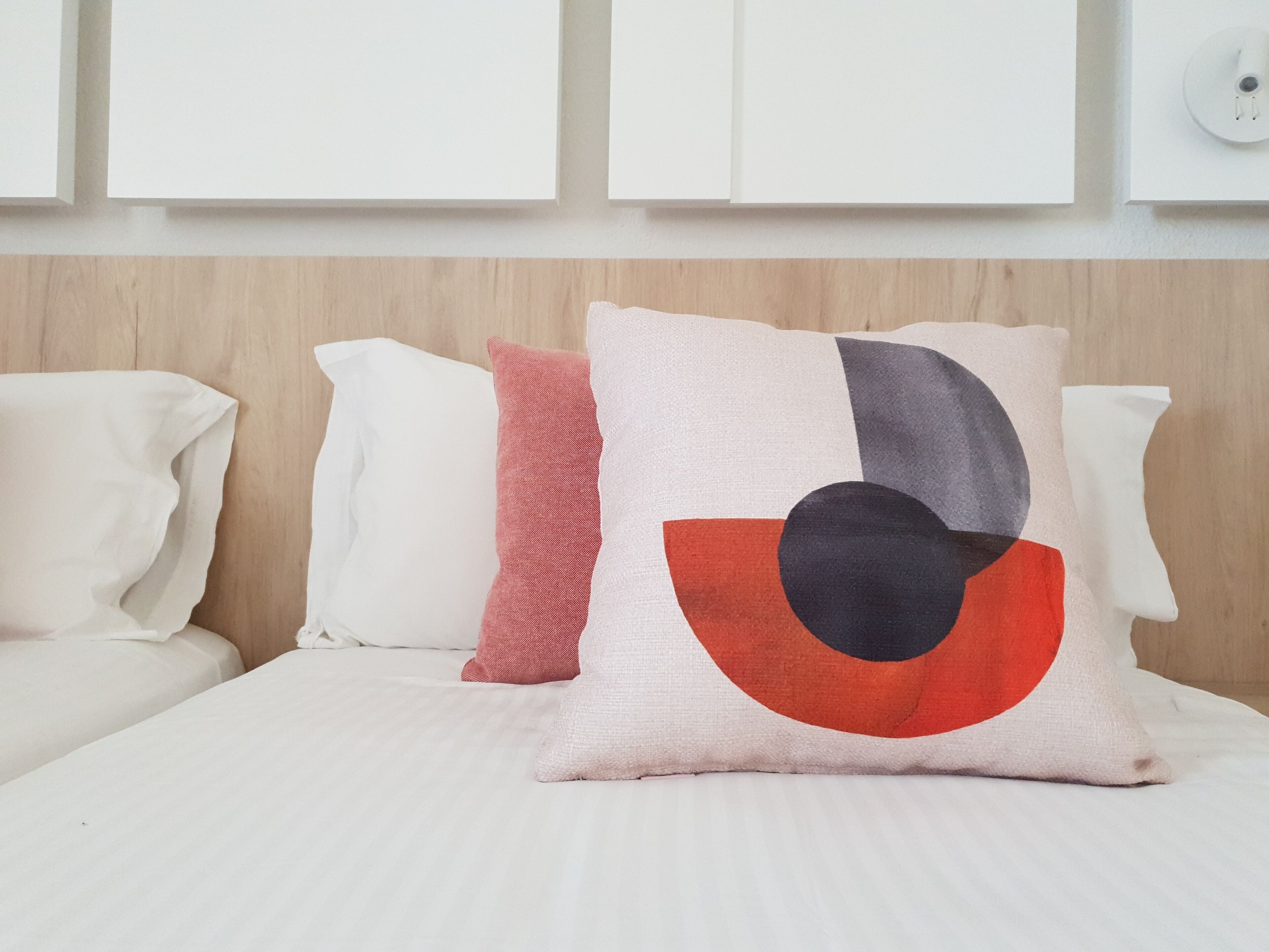 Una cama con ropa de cama y almohadas blancas, incluyendo una almohada roja y negra.