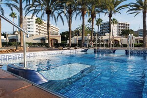 Una piscina con agua azul cristalina, rodeada de palmeras y edificios de hotel al fondo.