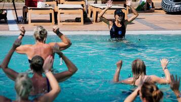 Una piscina con gente en el agua, sillas de descanso y un neumático al fondo.