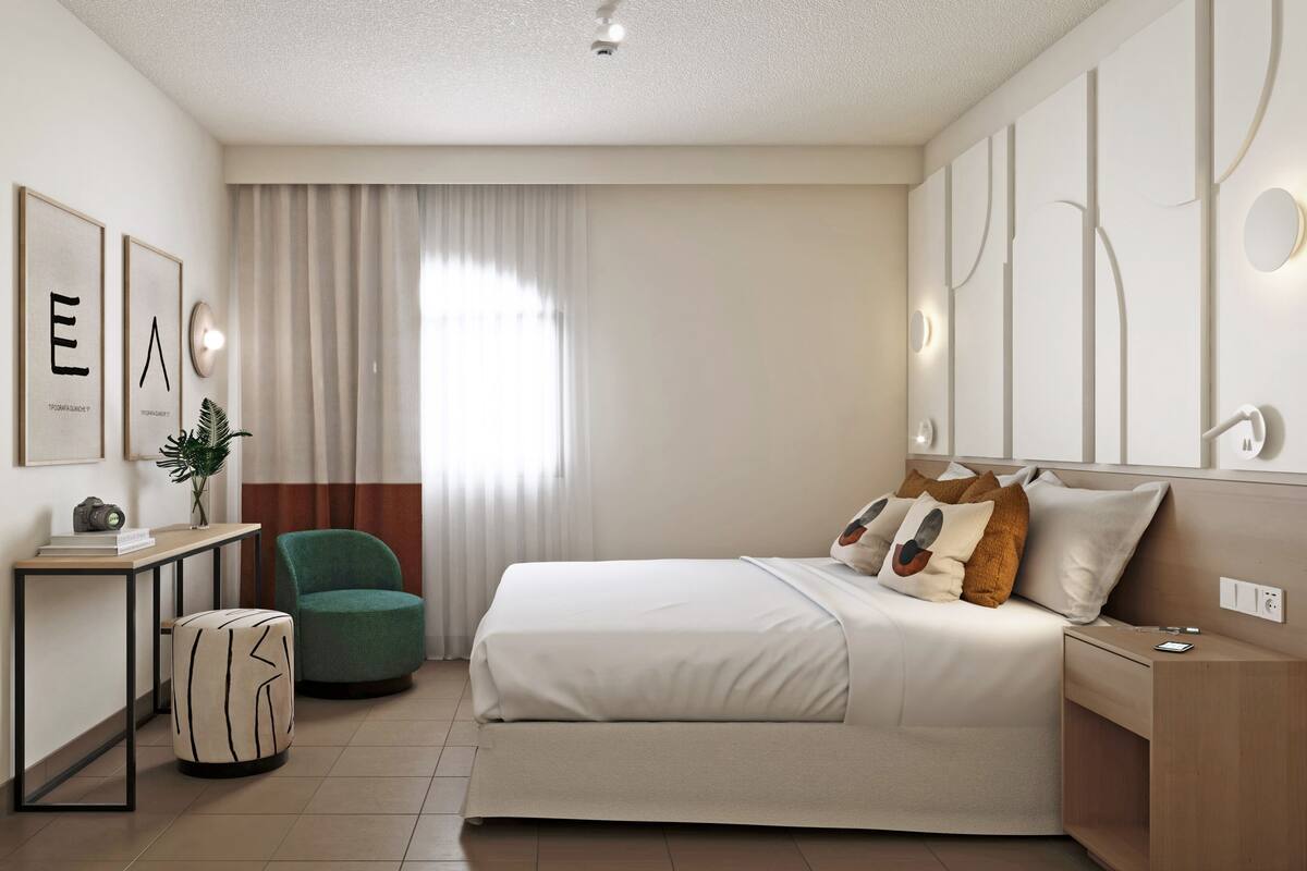 Une chambre d’hôtel moderne, dotée d’un grand lit, d’un bureau avec une chaise, d’un miroir et d’œuvres d’art accrochées aux murs.