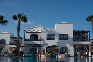 A modern hotel with a pool area, palm trees, and a clear blue sky.