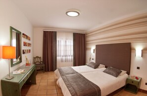 A hotel room with a bed, a desk, a chair, a lamp, and a window with curtains.