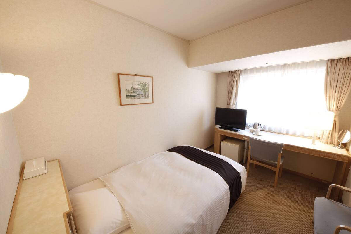 Een hotelkamer met een bed, een bureau met een computer, een televisie en een raam met gordijnen.