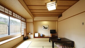 Ein traditioneller japanischer Raum mit Tatami-Böden, einem niedrigen Tisch mit Kissen, einem Fernseher und einem Shoji-Bildschirm.