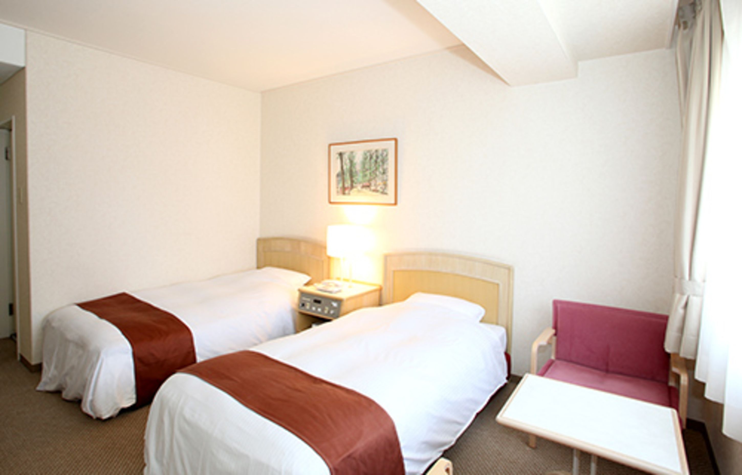 Une chambre d’hôtel avec deux lits, une petite table, une chaise et une table de chevet avec une lampe.