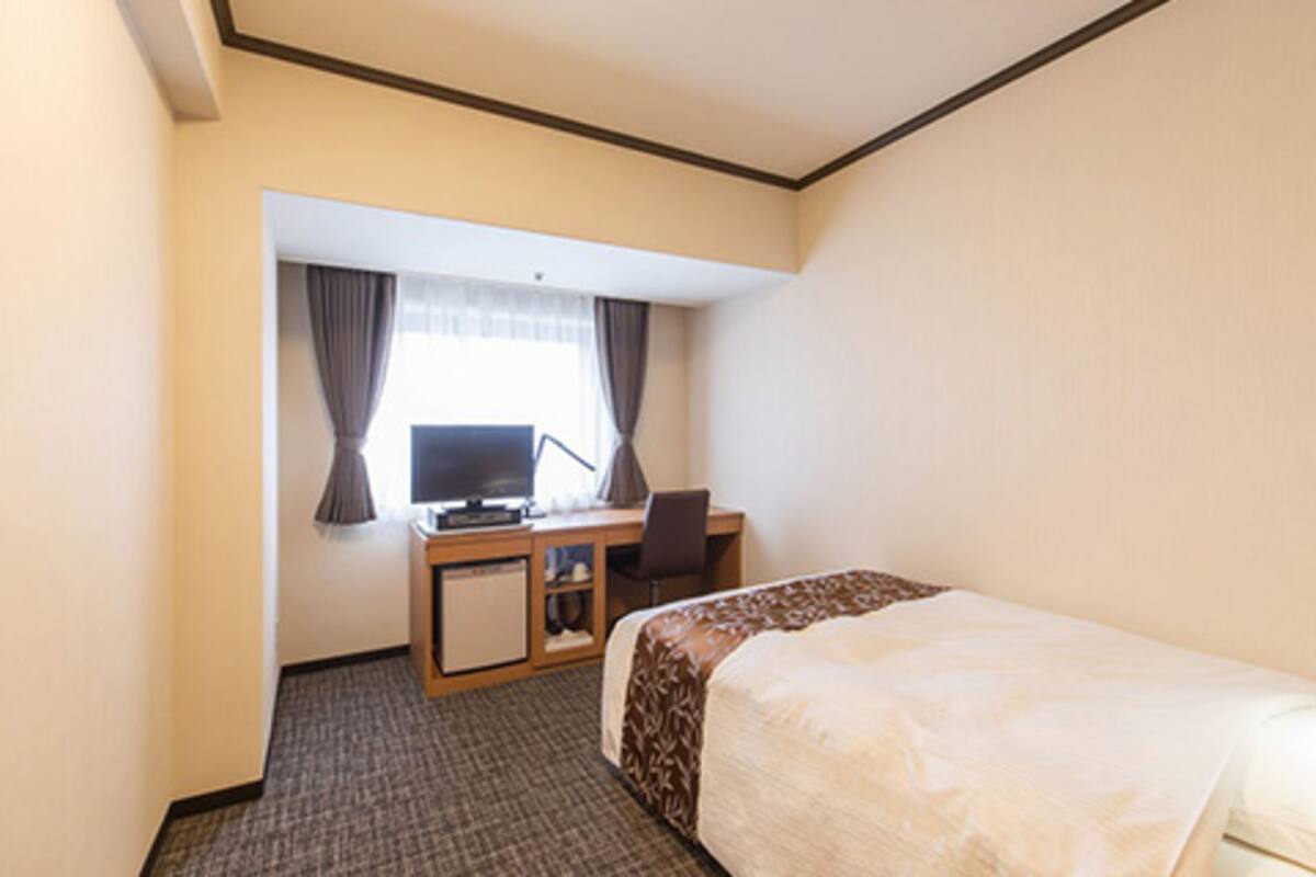 Hotelkamer met een bed, bureau, stoel, televisie en raam met gordijnen.
